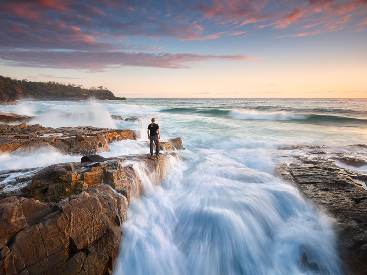 A man standing on the rocks of the Noosa coast, surrounded by waves