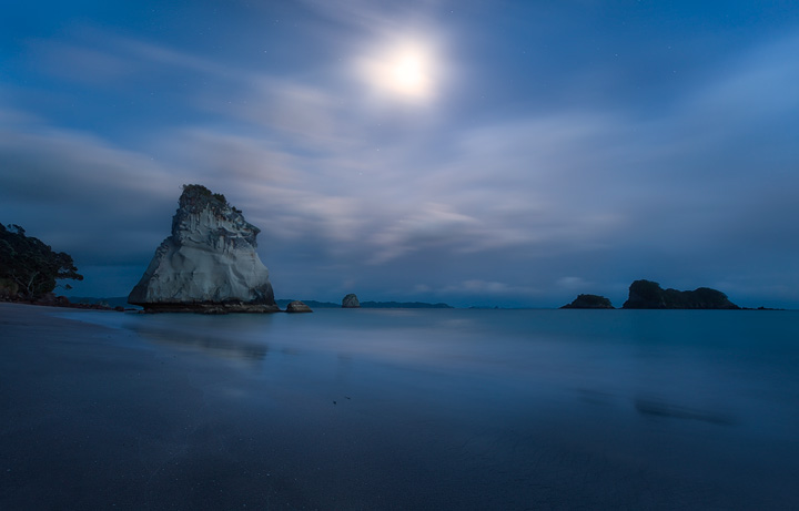 A full moon glimpses through the clouds at Cathedral Cove