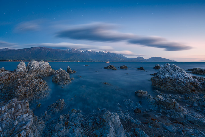 Snow capped mountains under a starry sky with calm sea in front