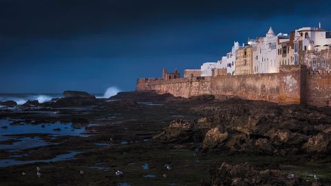 Essaouira White buildings and ancient fortress walls line the rocky Atlantic coastline in Essaouira, Morocco, under a dramatic dark sky.