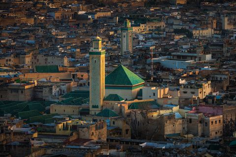 Fes Medina Aerial view of an old city with densely packed buildings, featuring a mosque with green-tiled roof and minarets prominently in the center.