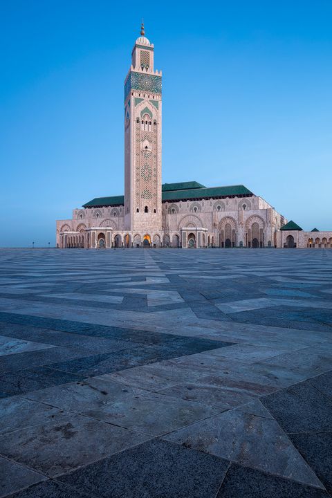Hassan II Blues Wide-angle view of the Hassan II Mosque in Casablanca, Morocco, featuring its grand minaret and expansive patterned stone plaza under a clear blue sky.
