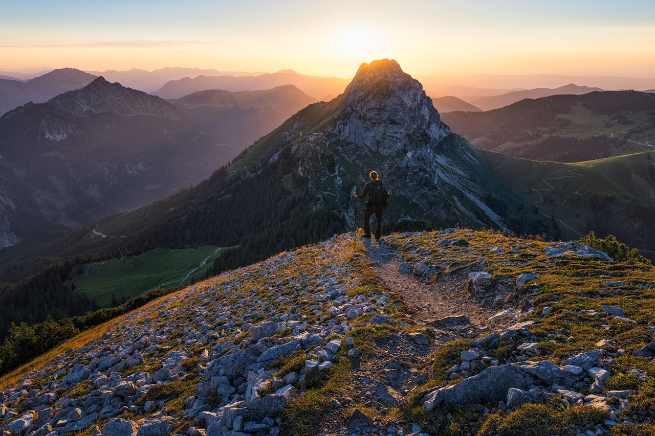 Ein Wanderer blickt zum Aggenstein und zur untergehenden Sonne.