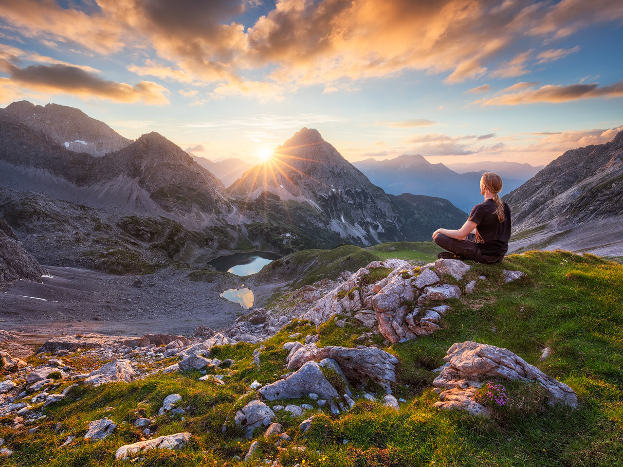 Eine Person meditiert in den Österreichischen Bergen mit der untergehenden Sonne.