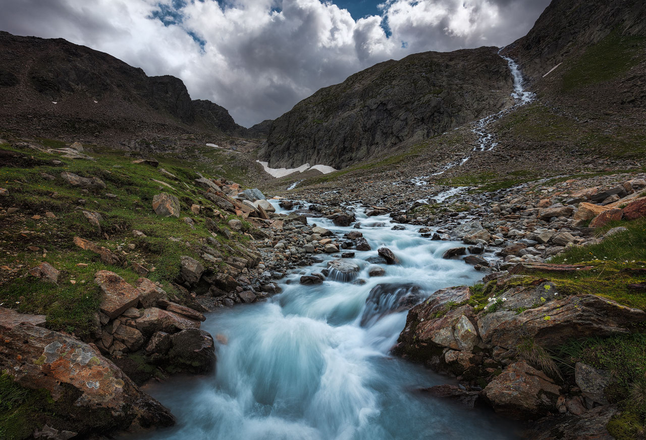A raging mountain stream in the Stubai Valley under a cloudy sky.