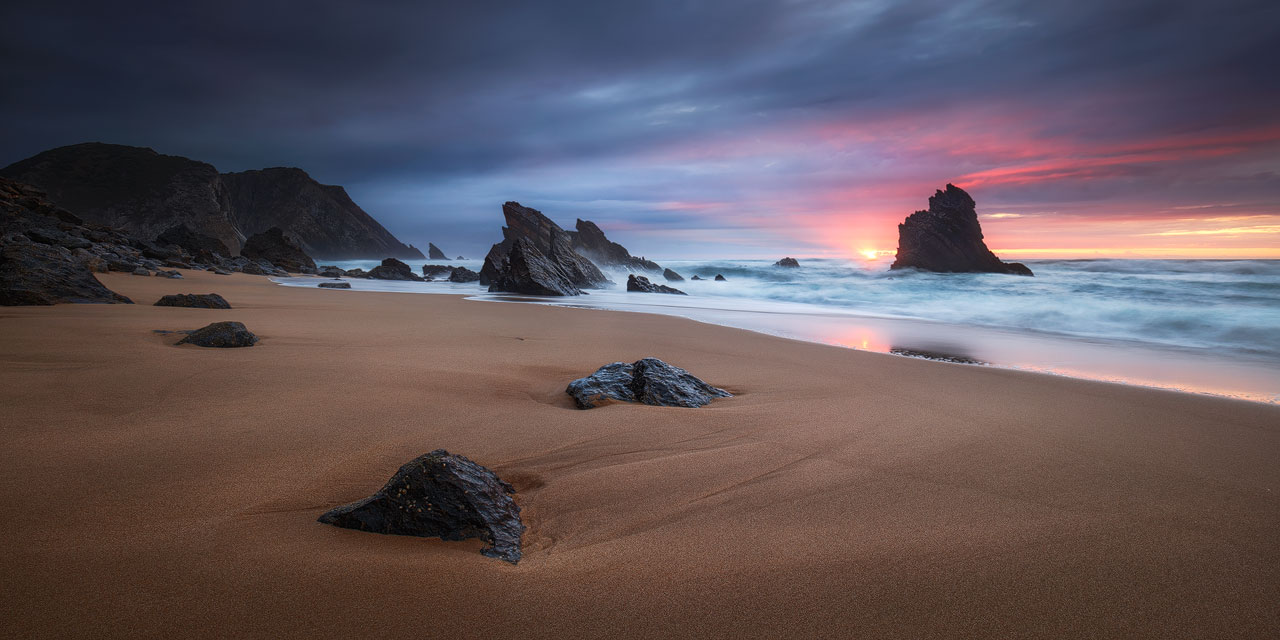Der Himmel glüht hinter den Felsen am Praia da Adraga in Portugal