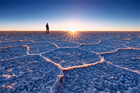 Ein Man steht in der endlosen Salzwüste und beobachtet den Sonnenuntergang