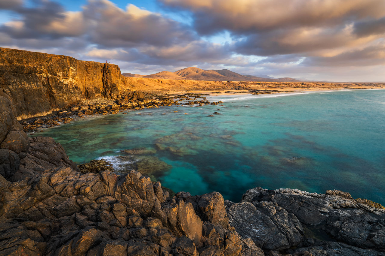 View along dramatic cliffs toward El Cotillo beach with warm sunset light.