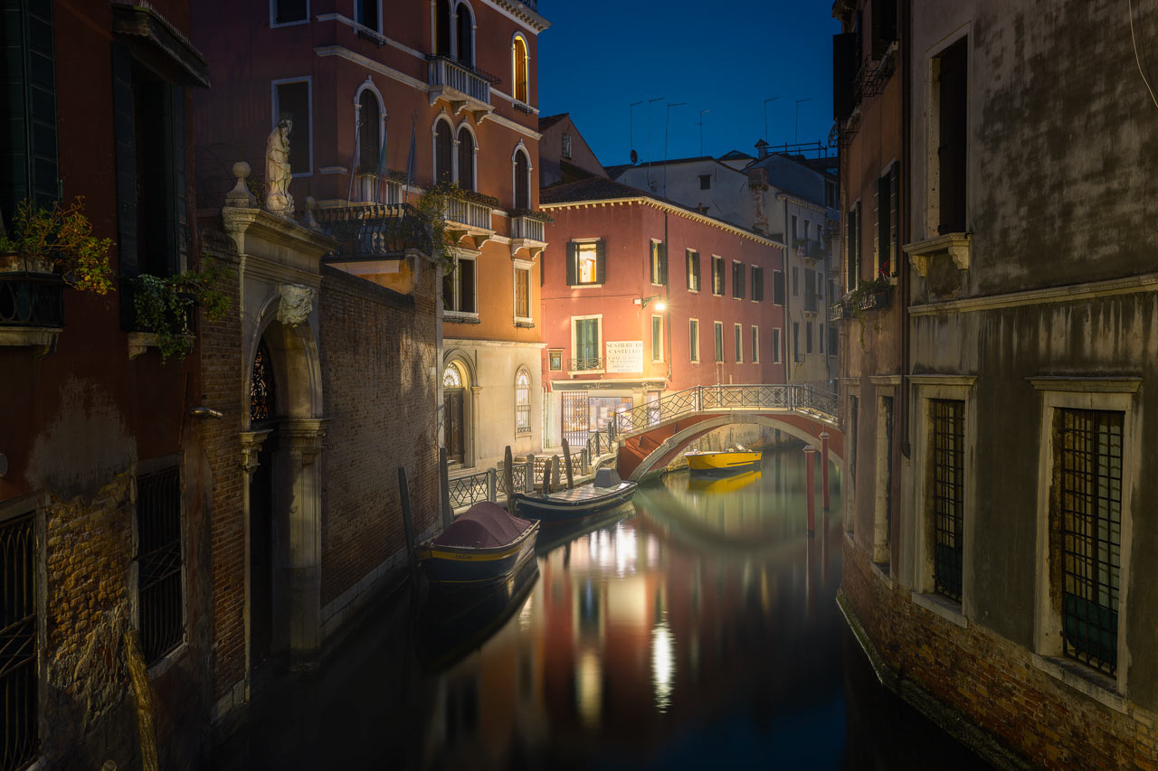 A moody evening in Venice with a misty, illuminated canal under a blue sky.